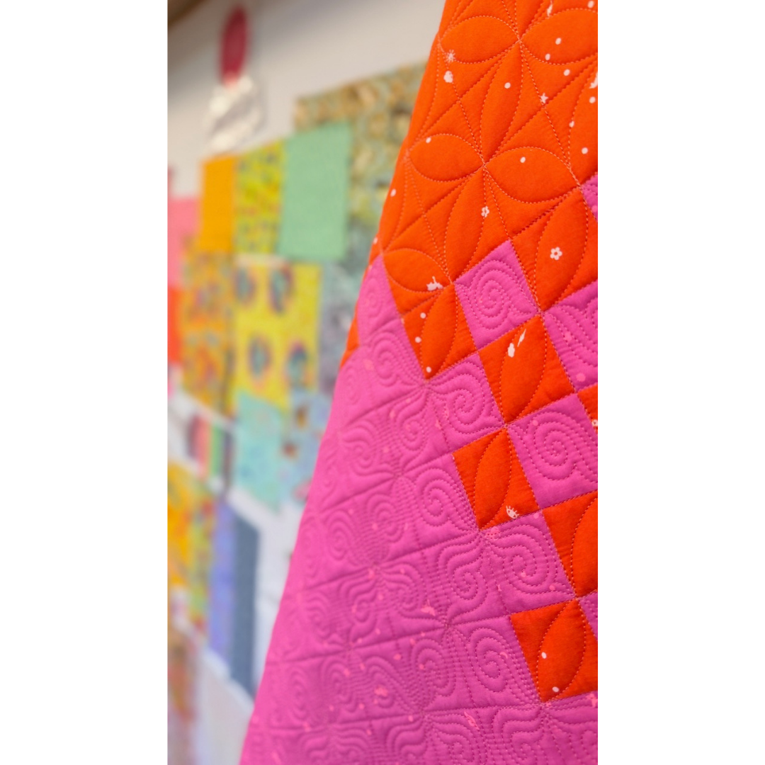 Close-up of a colorful quilt with geometric patterns, featuring orange, pink, and red colors.