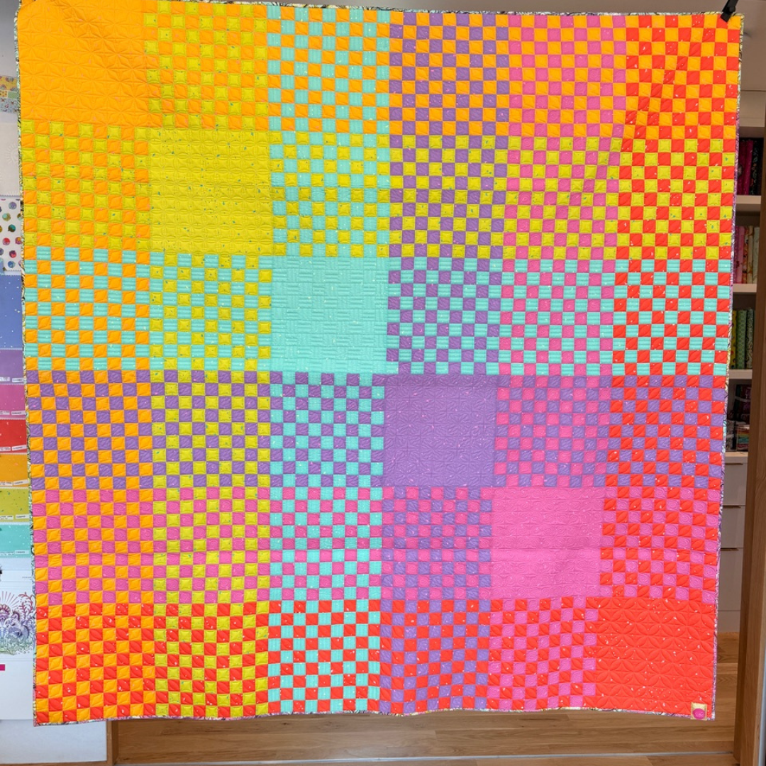 Colorful quilt with a geometric pattern draped over a wooden surface.