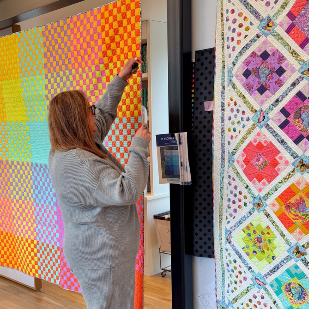 Person interacting with a colorful quilt display in a studio.