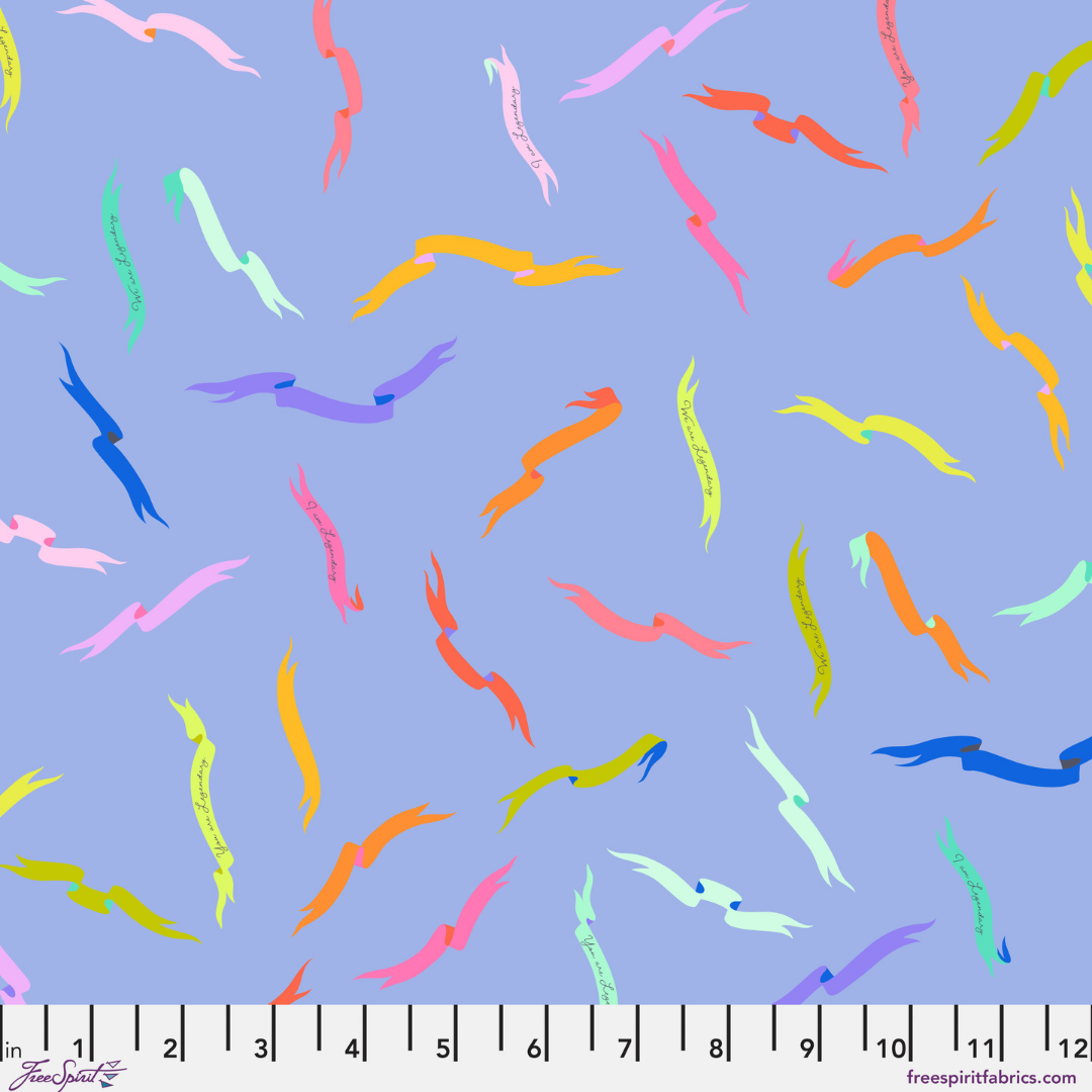 Fabric Swatch with a colorful tossed ribbon print on a soft periwinkle-blue background. The floating banners are bright, playful, and quietly encouraging, with tiny handwritten reminders like “You are Legendary,” “I am Legendary,” and “We are Legendary” tucked into the design. Has a ruler at the bottom.
